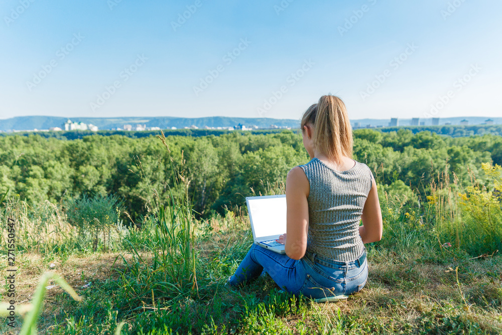 Girl with laptop on the nature on the background of forest and sky. The concept of combining leisure and work. Individual entrepreneur. Work at the computer away from the city. Girl with laptop on the nature on the background of forest and sky. The concept of combining leisure and work. Individual entrepreneur. Work at the computer away from the city.