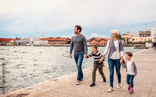 Young family with two small children walking outdoors on beach, holding hands. © Halfpoint