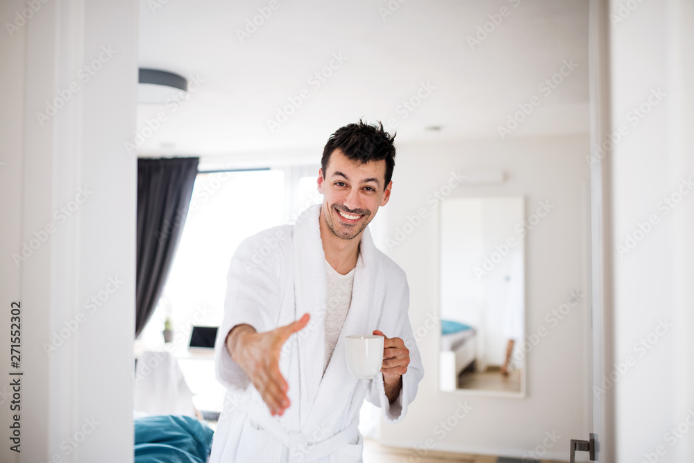 Young man with coffee offering hand for greeting in the bedroom, a morning routine.