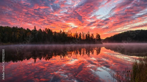 Clouds moving across a sunrise sky over a misty lake and forest