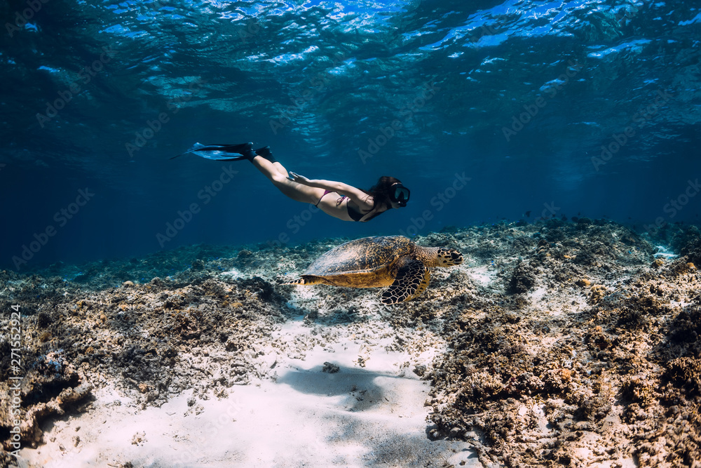 Woman freediver glides underwater with sea turtle.