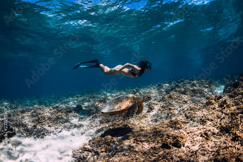 Young woman freediver glides underwater with sea turtle.