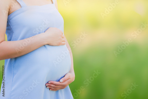 A pregnant woman in a blue dress on a nature background close-up. Pregnancy, parenthood, motherhood concept. Love for children concept with copy space.