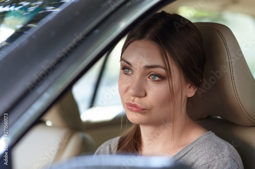 Young attractive caucasian woman behind the wheel driving a car with grimace of disappointment, frustration or displease. Strong emotions, duck face. Copy space.