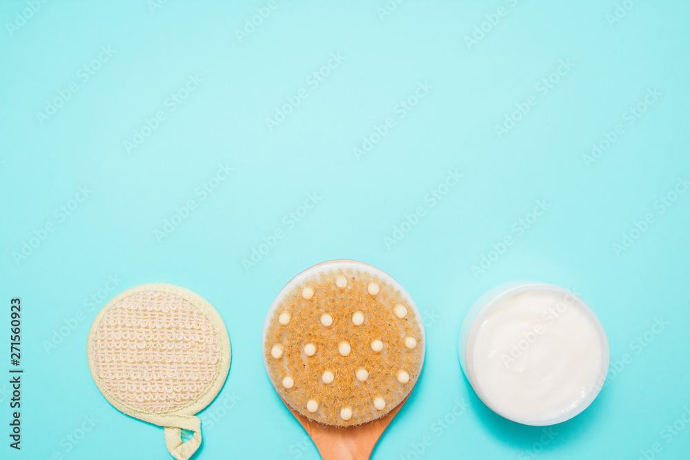 Body massage brush with cream on blue background. Massage brush for the body. Skin care products. Spa massage brush with natural bristles for body peeling or anti-cellulite massage. Top view. Body massage brush with cream on blue background. Massage brush for the body. Skin care products. Spa massage brush with natural bristles for body peeling or anti-cellulite massage. Top view.