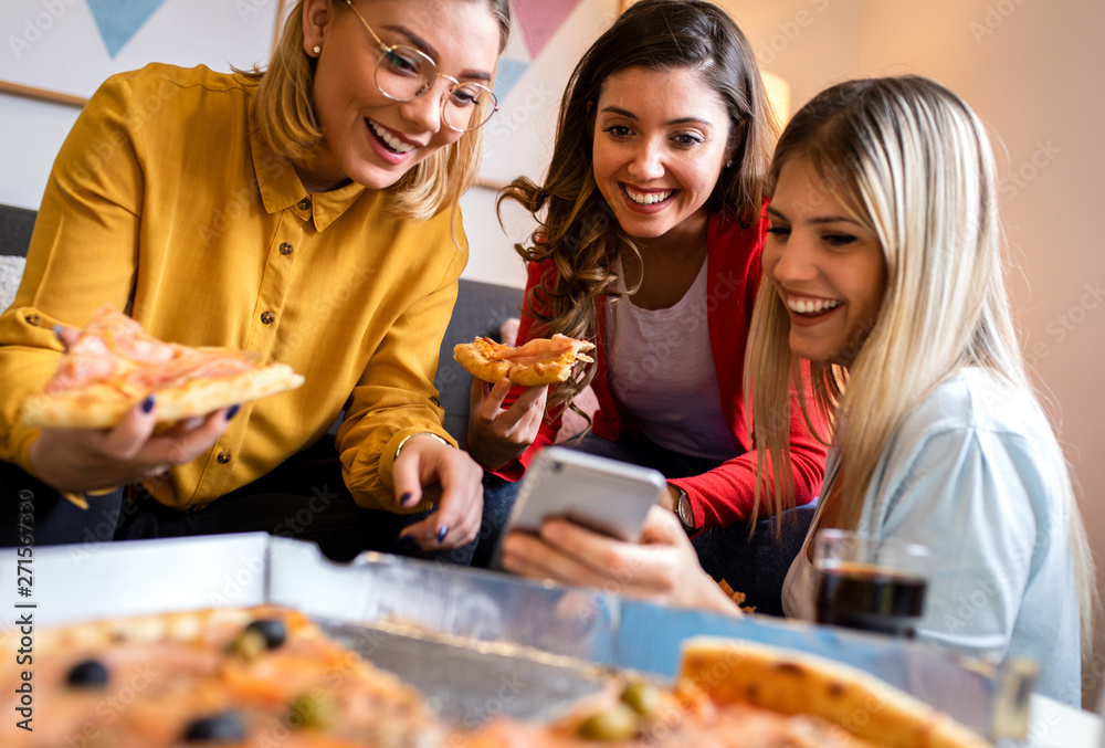 Three female friends chatting and enjoying eating pizza at home.