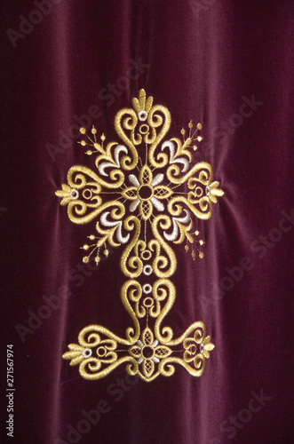 Cross embroidered with shiny gold thread on burgundy curtain in church in Greece