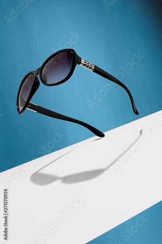 Front view shot of ink black oval-shaped sunglasses, adorned with silver criss-crossed insertions on ear-pieces. The tilted accessory is isolated in air against background with wide white stripe. photo