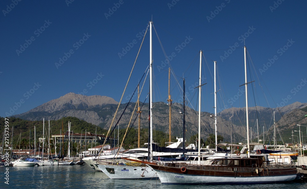 Motor boats at the pier on the sea. Mountains, coniferous forest and office in the background.