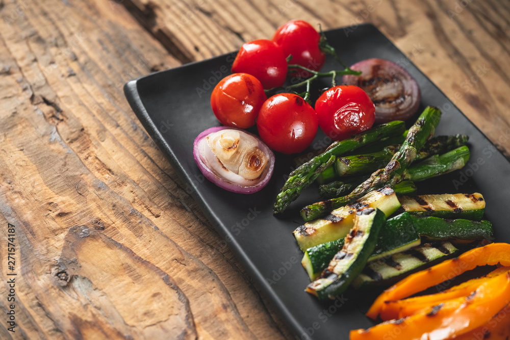 Grilled vegetables assorted on black plate on wooden table background, top view. Grilled vegetables assorted on black plate on wooden table background, top view.