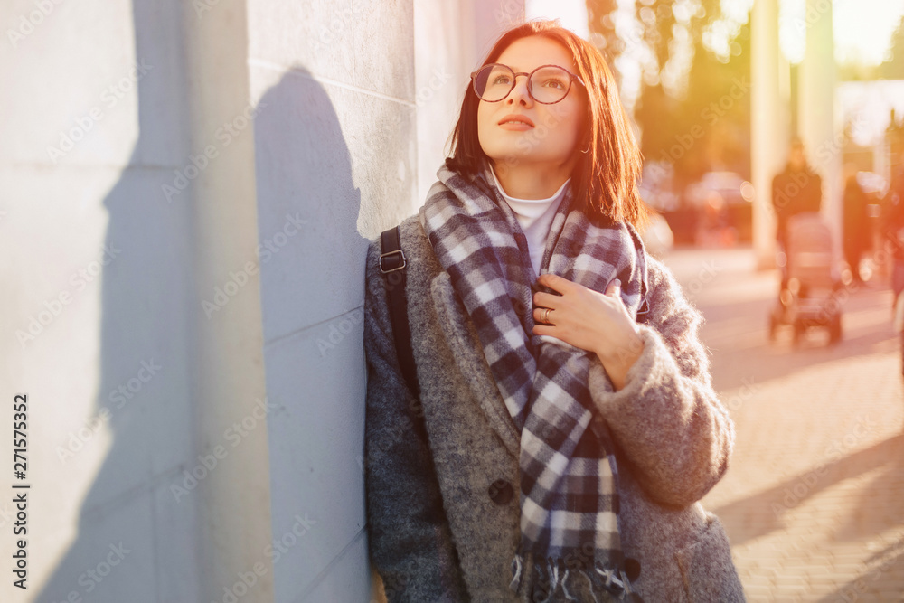 Attractive young girl wearing glasses in a coat walking on a sunny day