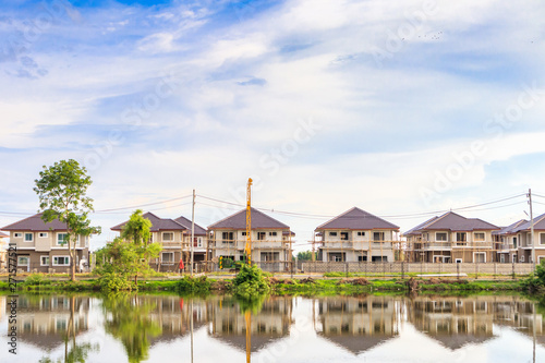 New house building reflection with water in lake at residential estate construction site with clouds and blue sky