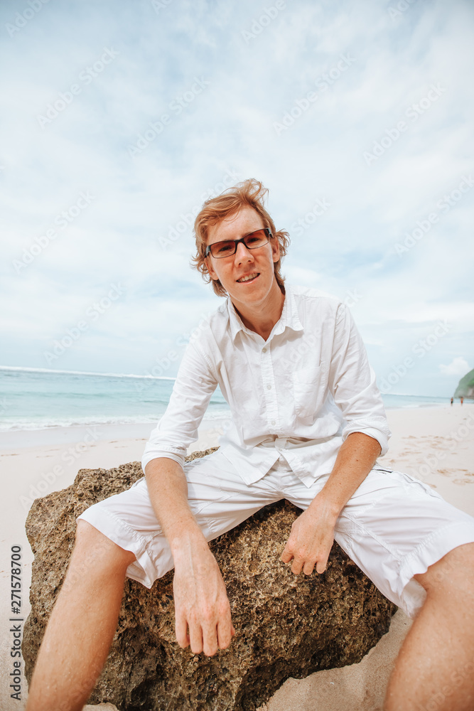 Portrait of a red-haired man in white clothes on a white beach in sunglasses