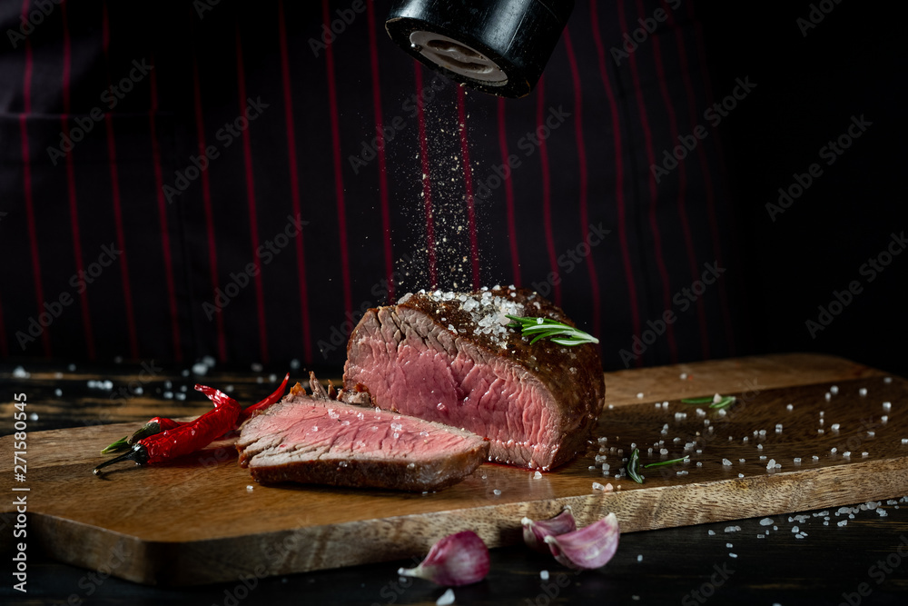 Cooking juicy beef steak by chef hands on dark black background with