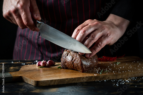 Fotografiet Meat steak slicing by knife in chef hands closeup