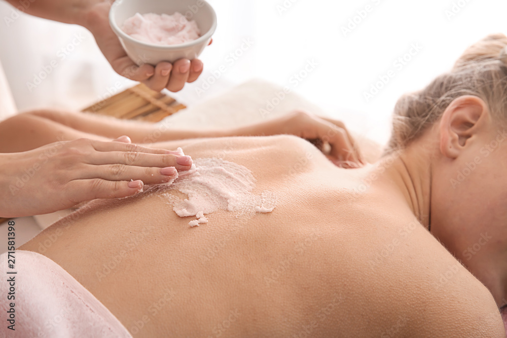 Fototapeta premium Young woman undergoing treatment with body scrub in spa salon