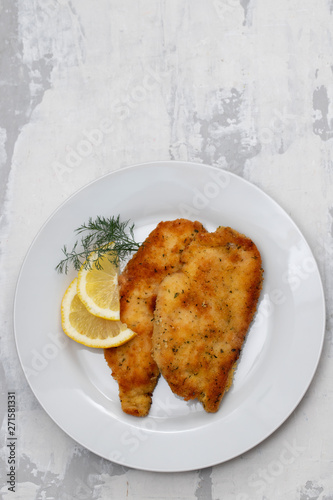 fried chicken with lemon on white plate on ceramic background