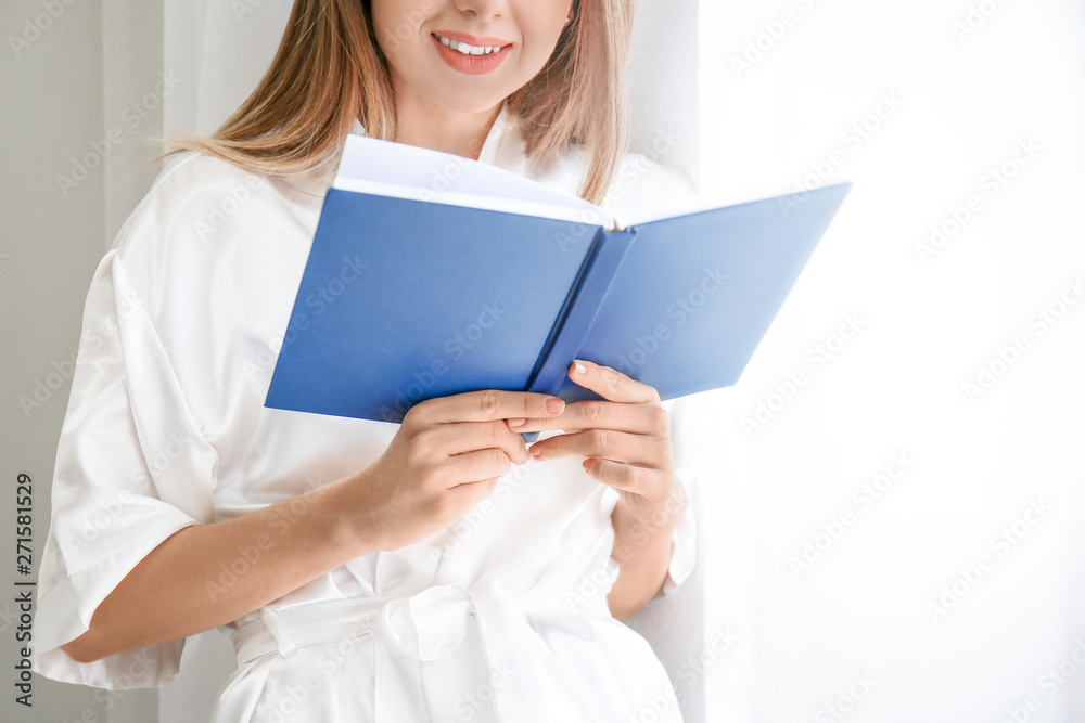 Beautiful young woman reading book near window Beautiful young woman reading book near window
