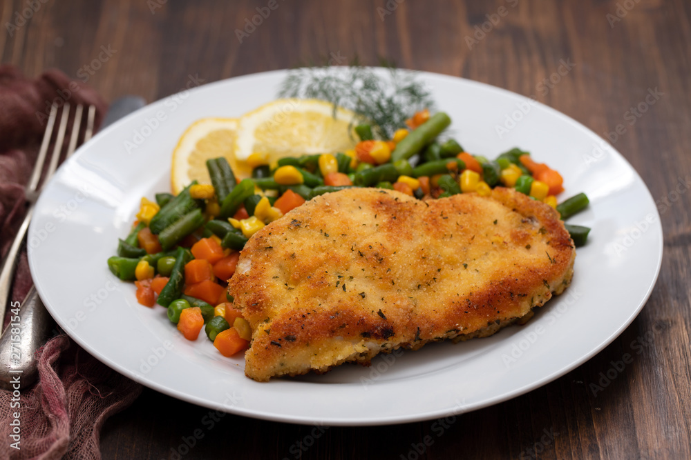 fried chicken with boiled vegetables and lemon on white dish