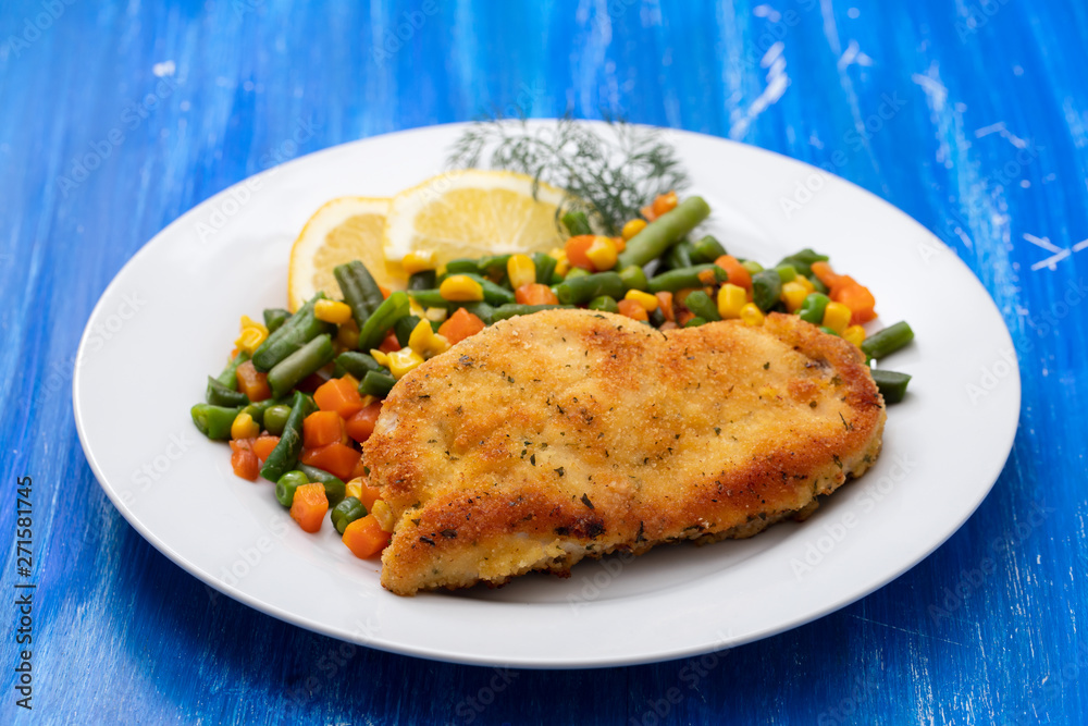 fried chicken with boiled vegetables and lemon on white dish