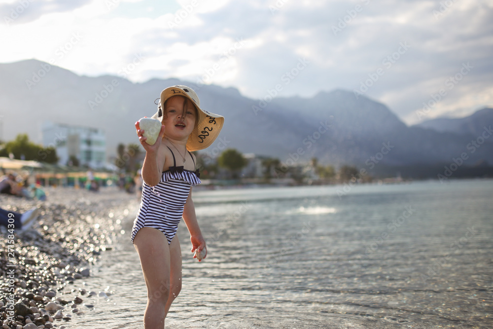 child in striped swimsuit and hat splashing in sea