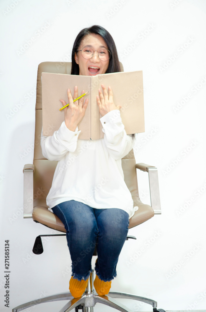 The woman wore a white shirt, wearing glasses on the chair, yellow socks, holding a pencil and a book. She was smiling.Brown books in Asian women hands. The woman wore a white shirt, wearing glasses on the chair, yellow socks, holding a pencil and a book. She was smiling.Brown books in Asian women hands.