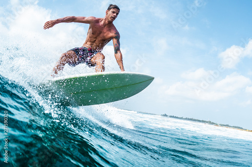 Fotografia Young surfer with lean muscular body rides the tropical wave