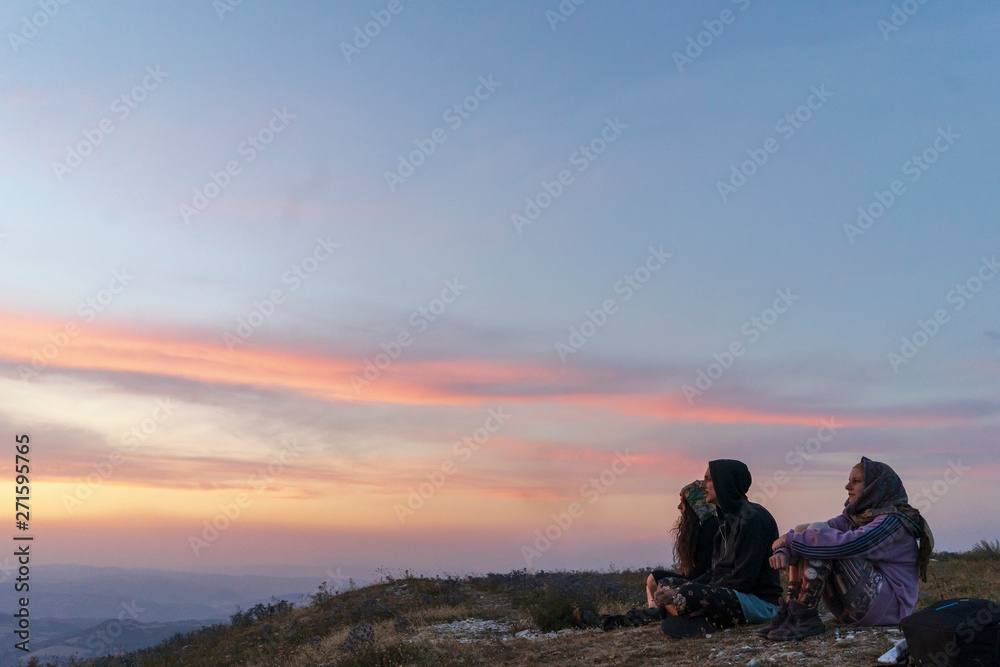 Group of friends watching the sunset sitting on the top of a mountain