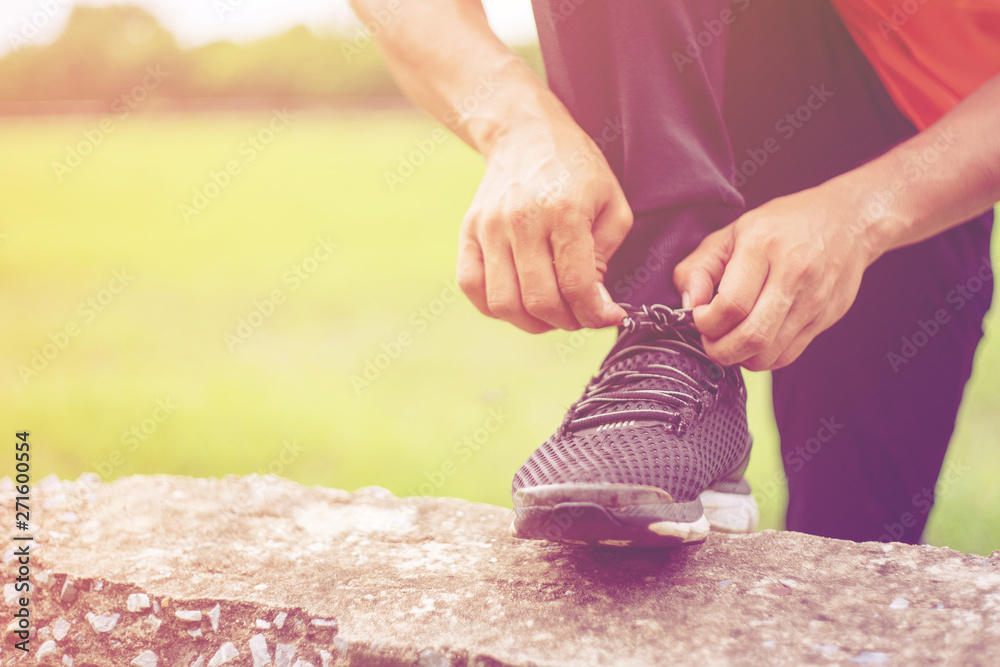 Close up of a male runner tights shoe laces preparing for jogging outdoors. Cropped shot of a man tights his shoelaces before running in the park in the evening. Sport and recreation concept.
