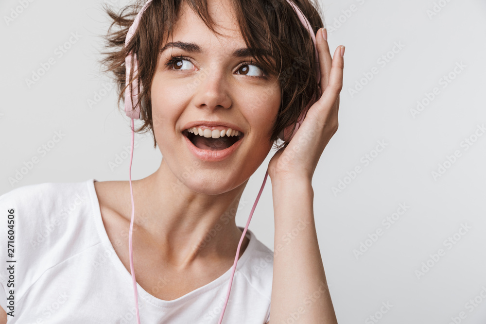 Pretty excited happy woman posing isolated over white wall background listening music with headphones. Pretty excited happy woman posing isolated over white wall background listening music with headphones.
