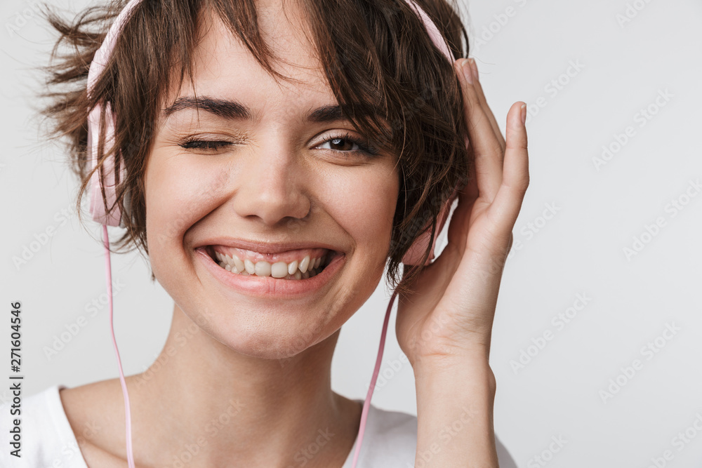 Pretty excited happy woman posing isolated over white wall background listening music with headphones. Pretty excited happy woman posing isolated over white wall background listening music with headphones.