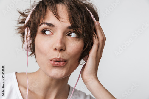 Pretty excited happy woman posing isolated over white wall background listening music with headphones.