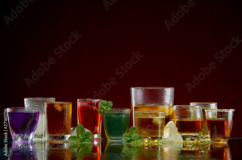 Different alcoholic drinks in clear glasses with ice and mint on red background