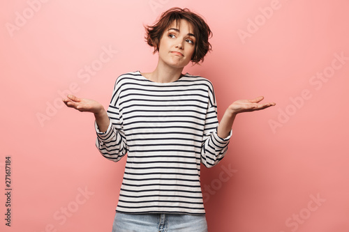 Confused unsure beautiful woman posing isolated over pink wall background. photo