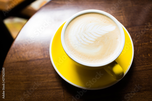 Yellow cup of aromatic coffee on a wooden table.