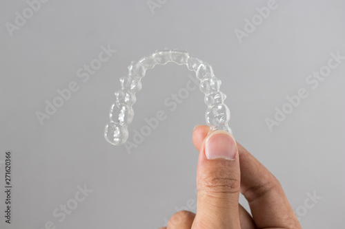 Holding invisalign braces or invisible retainers on grey background, new orthodontic equipment
