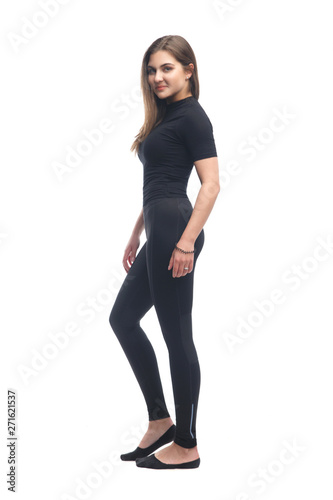 Slender brunette girl in black tight clothes standing isolated on white background.