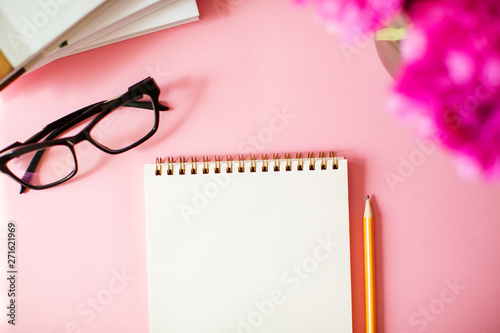 Notebook with pencil and glasses on pink background.