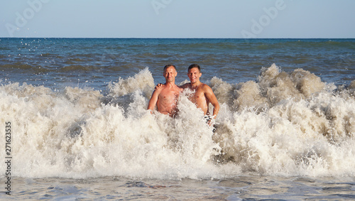 Two sun-tanned man in surf waves on the beach