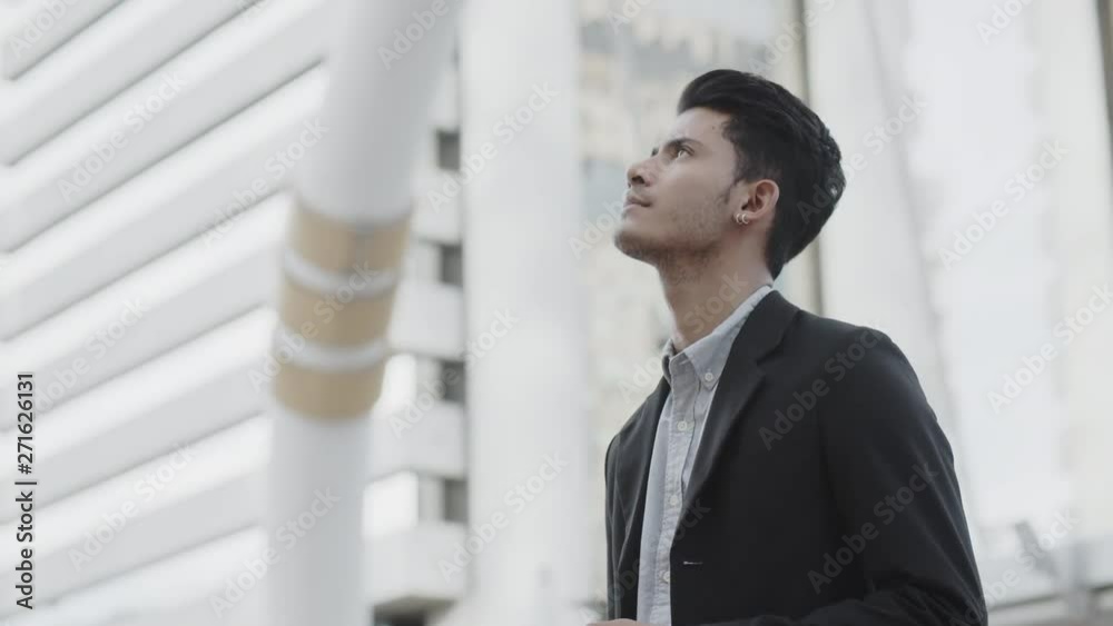 The image of a young Asian businessman standing at Outside Office, smiling and using the phone. For discussion The image of a young Asian businessman standing at Outside Office, smiling and using the phone. For discussion