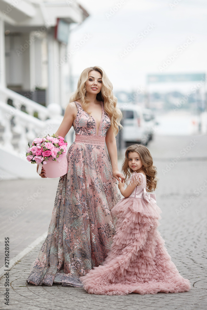 Beautiful slender woman and her little daughter,having fun together outdoors in the spring,on a palace alley with flowering peaches,dressed in beautiful ball gowns of pink color. Beautiful slender woman and her little daughter,having fun together outdoors in the spring,on a palace alley with flowering peaches,dressed in beautiful ball gowns of pink color.