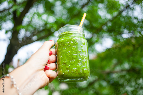 woman's hand holding jar with green cold-pressed juice, vegetable garden background. Healthy eating, detoxing, juicing, body cleancing concept photo