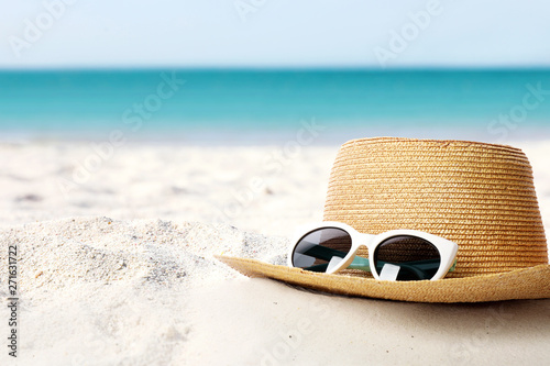 Hat and sunglasses on sand near sea, space for text. Stylish beach accessories