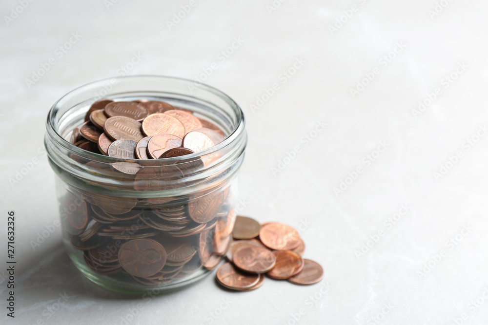 Glass jar and coins on light background. Space for text Glass jar and coins on light background. Space for text
