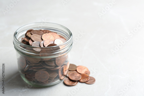 Glass jar and coins on light background. Space for text