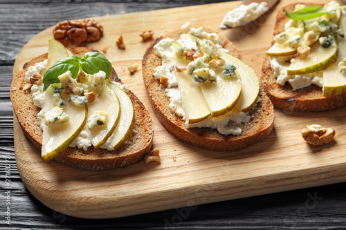 Wooden board with delicious pear bruschettas on table, closeup