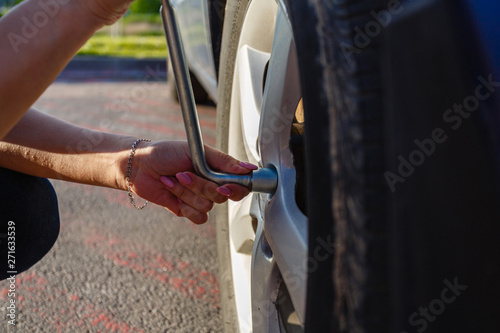Closeup young woman's hands with good manicure changes wheel on highway using cylinder key to unscrew damaged car wheel. Woman changes flat wheel after her car breaks down. Concept installation tires