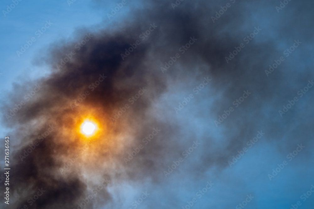 Black Smoke against sunlight blue sky from burning in hottest weather. Weather and pollution concept.