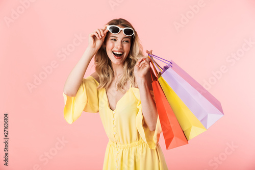 Beautiful happy young blonde woman posing isolated over pink wall background holding shopping bags. photo