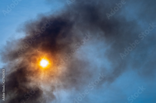 Black Smoke against sunlight blue sky from burning in hottest weather. Weather and pollution concept.